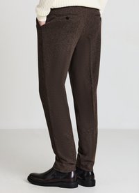 Braune, strukturierte Hose mit Seitentaschen, schmaler Passform und Knopfdetails. Kombiniert mit schwarzen Schuhen für einen eleganten Look.