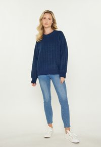 Maglione navy a trecce con scollo rotondo e maniche lunghe, abbinato a jeans skinny blu chiaro e sneakers bianche.