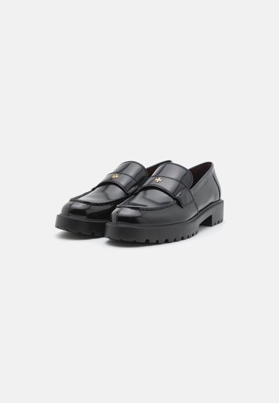 Mocasines de cuero negro con un acabado brillante, que presentan una correa frontal, un pequeño emblema dorado y una suela negra gruesa y texturizada.