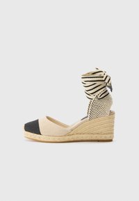 Wedge espadrille med en beige og svart canvas kropp, stripet stoff ankelbånd og en flettet jute såle. Lukket tå med teksturerte detaljer.