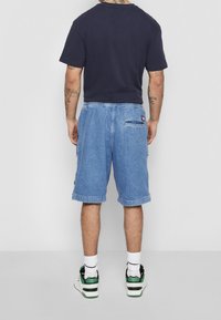 Shorts de mezclilla en azul claro con un corte relajado, que cuentan con un bolsillo trasero y una cinturilla elástica. Combinados con una camiseta oscura y zapatillas.