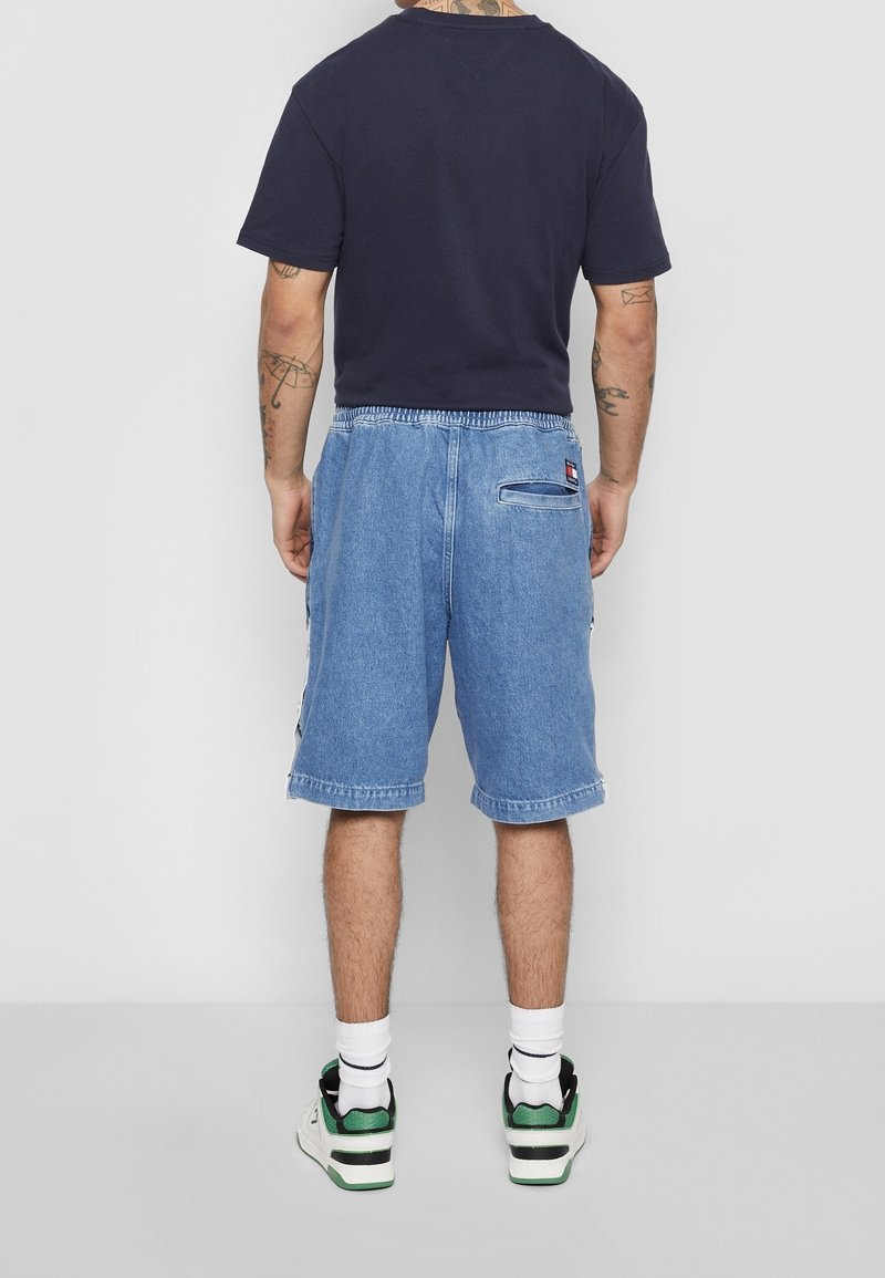 Shorts de mezclilla en azul claro con un corte relajado, que cuentan con un bolsillo trasero y una cinturilla elástica. Combinados con una camiseta oscura y zapatillas.