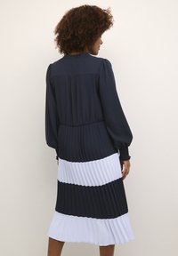 Gari ar līkumiem un garām piedurknēm, ar tumši zilu un baltu svītru dizainu, elastīgu jostasvietu, teksturētu audumu un gludu augšdaļas dizainu.