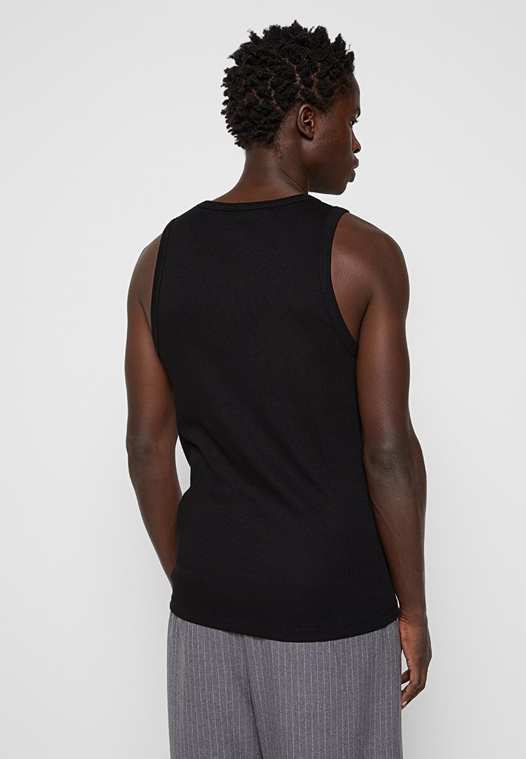Top negro sin mangas con textura acanalada, que presenta un escote redondo y una silueta ajustada, combinado con pantalones a rayas gris claro.