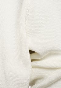 Gros plan d’un tissu tricoté blanc texturé plié pour montrer les détails des coutures et du tissage.