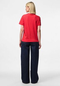 Rød bomulds T-shirt med rund hals, parret med brede mørkeblå denim jeans. Stofmet ser glat ud med en behagelig pasform.