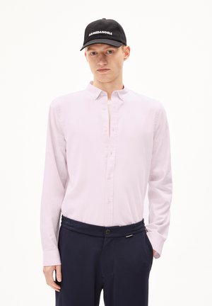 Lichtroze overhemd met knopen en een puntig boord, gecombineerd met marineblauwe broek met een geribde tailleband en knoopsluiting. Zwarte pet met wit logo.