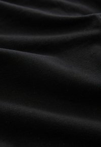 Schwarzer Stoff mit einer glatten, leicht dehnbaren Textur, die sanfte Falten und ein gleichmäßiges mattes Finish zeigt. Keine Muster oder sichtbaren Hardware-Details.