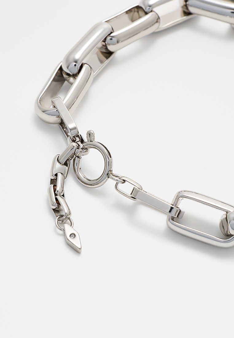 Collier en chaîne argentée avec des maillons de formes variées, doté d'un fermoir à pince en forme de homard et d'une petite étiquette avec un trou pour attachement.