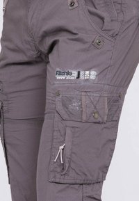 Pantalons cargo gris avec une finition texturée, présentant plusieurs poches, des fermetures à pression et un détail de logo sur la jambe.