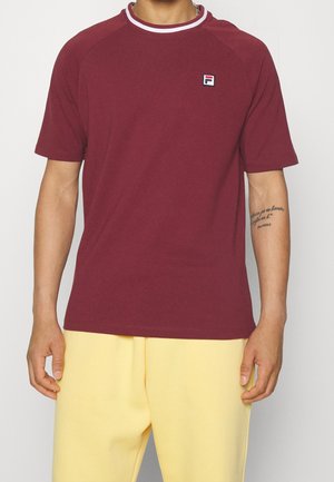 Mørkerød T-shirt med korte ærmer og en hvid og rød ribbet krave, med Fila-logoet på venstre bryst. Blødt, tekstureret stof.