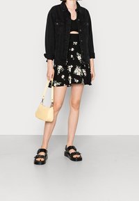 Giacca di jeans nera, top corto nero, gonna floreale nera, borsa gialla testurizzata e sandali platform neri con fibbie.