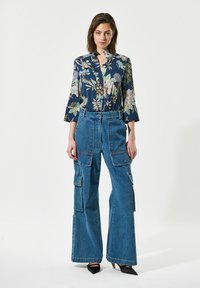 Blusa navy con motivo floreale e maniche a tre quarti abbinata a pantaloni cargo blu in denim a gamba larga con molteplici tasche e vita alta.