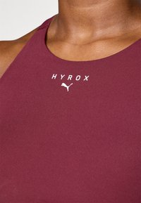 Maroon sports tank top with a rounded neckline, featuring the text "HYROX" and a white Puma logo on the front. Smooth, stretchy fabric.