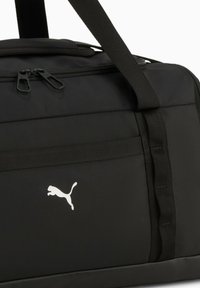Sort Puma sportstaske med dobbelt lynlåse, bærereimer og hvidt Puma-logo på frontlommen.