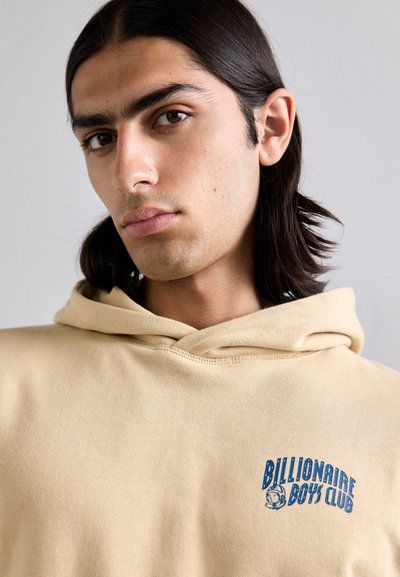 Kreminės spalvos su gobtuvu sportinė palaidinė su mėlynu "Billionaire Boys Club" logotipu, pagaminta iš minkštos medžiagos, su laisvu kirpimu ir matomomis siūlėmis.
