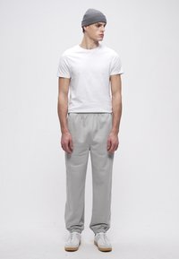 Szürke szabadidőnadrág gumis derékrésszel, hozzáillő, testhezálló fehér pólóval és szürke kötött sapkával; fehér sportcipővel viselve.