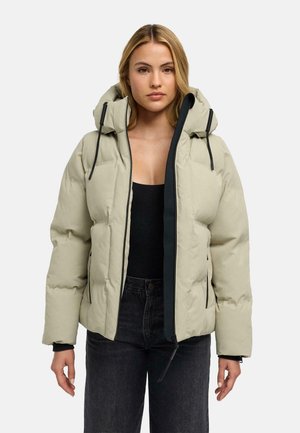 Kvinde iført en lysebeige dynejakke med stor hætte, sorte snore, sort foring og sorte jeans.
