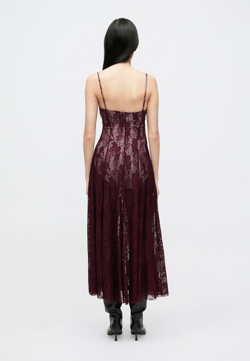 Robe maxi en dentelle bordeaux avec bretelles fines réglables, corsage cintré et jupe fluide. Texture transparente avec motifs floraux et design en couches.