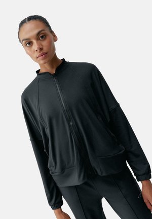 Schwarze Zip-Jacke mit hohem Kragen, lockerer Passform und Raglanärmel. Glatter, dehnbarer Stoff mit Seitentaschen und elastischen Bündchen.