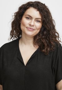 Sort bluse med et struktureret bølget mønster, der har V-udskæring og korte ærmer, designet til en afslappet pasform.