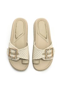 Sandales à glissière beiges avec une lanière en tissu tissé, ornées d'une boucle en strass carrée. Semelle plate avec un design minimaliste et une texture légère.