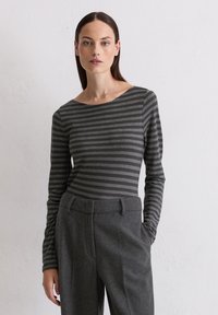 Dlhý rukáv, sivý pruhovaný top so širokým výstrihom, skombinovaný s vysokými sivej nohavicami vyrobenými z mäkkej, texturovanej tkaniny.