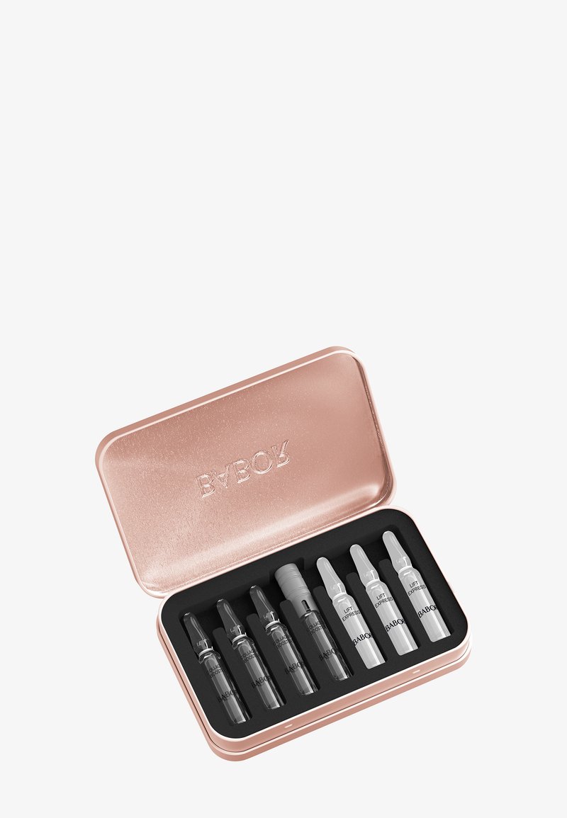 Boîtier en métal couleur or rose contenant huit petites ampoules cosmétiques, sept foncées et une claire, disposées dans une mousse noire.
