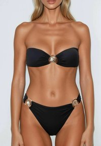 Set bikini nero con top senza spalline decorato con un accento a forma di conchiglia dorata al centro, e un perizoma a vita bassa con hardware a forma di conchiglia coordinato sui lati.