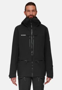 Schwarze wasserdichte Jacke mit hohem Kragen, verdeckten Reißverschlussverschlüssen, mehreren Taschen und einem Logo auf der Brust. Glatte Textur, funktionales Design.