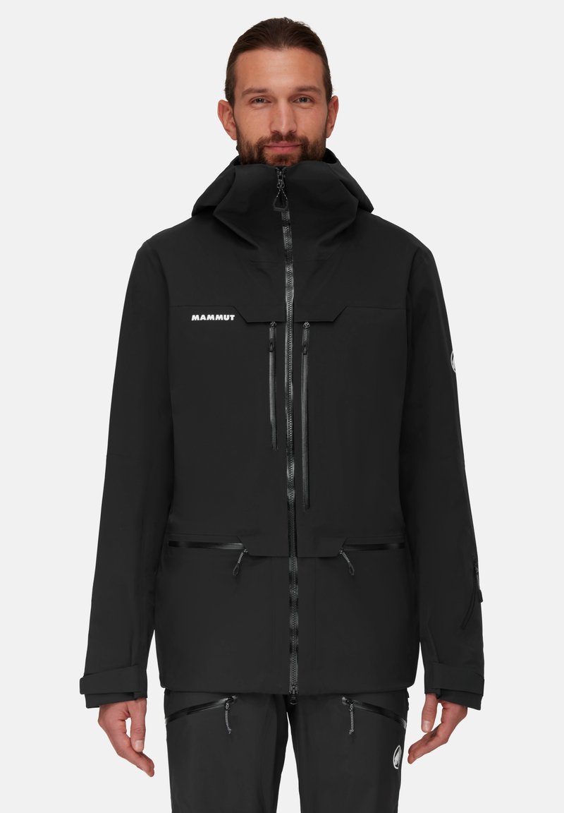 Schwarze wasserdichte Jacke mit hohem Kragen, verdeckten Reißverschlussverschlüssen, mehreren Taschen und einem Logo auf der Brust. Glatte Textur, funktionales Design.