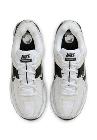Nike Vomero 5 superge v beli mrežasti tkanini z črnimi poudarki, ki imajo okrogle vezalke, oblazinjene podplate in oznako z znamko na jeziku.