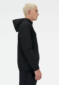 Giacca nera con cappuccio realizzata in tessuto liscio e leggero. Presenta un elastico in vita e nei polsini, con chiusura a zip e design minimalista.