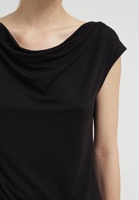 Top negro drapeado con un escote amplio y mangas cortas, confeccionado en una tela suave con un corte relajado y una sutil textura.