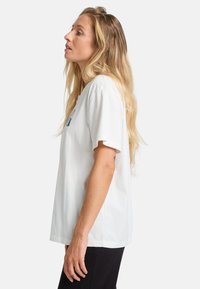 Hvid bomulds t-shirt med korte ærmer, afslappet pasform, rund halsudskæring, og blå grafisk tekst på fronten. Glat tekstur, enkelt design.