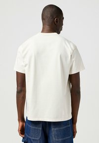 Camiseta de algodón blanca con manga corta, cuello redondo y dobladillo recto. Textura suave, silueta ajustada, sin patrones ni acentos visibles.