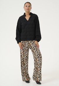 Blusa nera con texture, scollatura a V e colletto volante, abbinata a pantaloni larghi in stampa leopardata beige e nera. Ballerine nere.