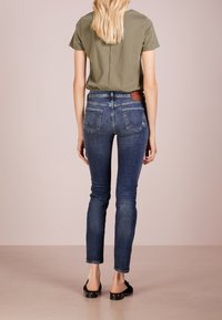 Denimjeans i mörkblått med smal passform och blekt struktur. Matchas med en olivgrön skjorta med kort ärm, synliga bakfickor.