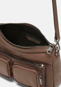 Borsa a tracolla in pelle marrone con scomparti con cerniera, un accento in metallo argentato e una texture morbida; l'interno presenta una fodera in tessuto scuro.