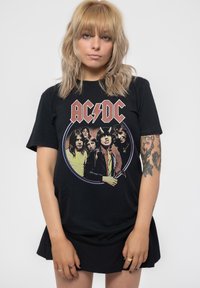 Black cotton t-shirt featuring a colorful AC/DC graphic print of band members in a circular design. Model wears a black skirt.