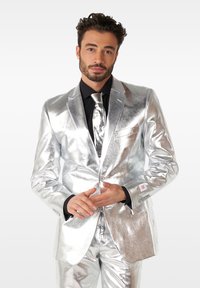 Silver metallic suit with shiny fabric, featuring a tailored fit, single button closure, and matching tie. Black shirt beneath adds contrast.