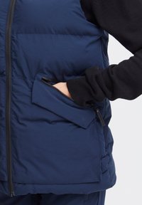 Mornarska puffer prsluk s detaljem zippered džepa s lijeve strane, s glatkom teksturom i zip zatvaranjem sprijeda.