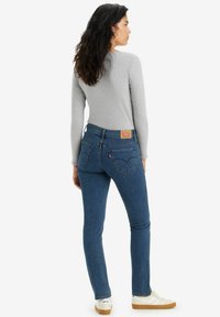 Jeans in denim blu skinny con vita alta e cinque tasche, abbinati a un top aderente a maniche lunghe grigio chiaro e sneakers bianche.