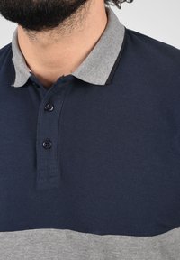 Sötétkék polo ing világosszürke gallérral és szürke csíkkal a mellrészen. Két gombbal és textúrázott anyaggal rendelkezik.