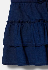 Tissu superposé bleu foncé avec un détail de volant froncé, montrant la texture et les coutures sur une section de vêtement.