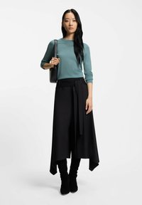 Lichtgroenblauw shirt met lange mouwen, gecombineerd met een zwart rokje met hoge taille en een strikceintuur, en zwarte stoffen kniehoge laarzen.