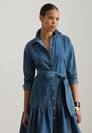 Sukienka dżinsowa z kołnierzykiem, długimi rękawami, talią zebrana w fałdy i spódnicą w kształcie litery A. Z przodu zapinana na guziki, z paskiem wiązanym w talii.