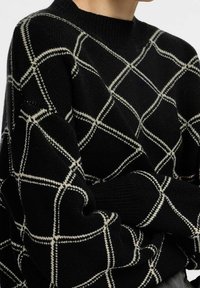 Svart stickad tröja med ett geometriskt vitt rutmönster. Har rundad halsringning och ribbad muddar. Texturerat tyg med lös passform.