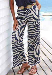 Wide-leg trousers in beige with navy zebra stripes. Lightweight fabric, elastic waistband, side pockets, paired with a metallic-accented belt.