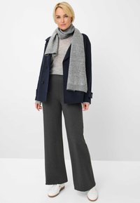 Marineblauer Peacoat, grauer Strickschal, hellgrauer Pullover und weite, dunkelgraue Hose, kombiniert mit weißen Sneakers. Strukturelle Stoffdetails sichtbar.